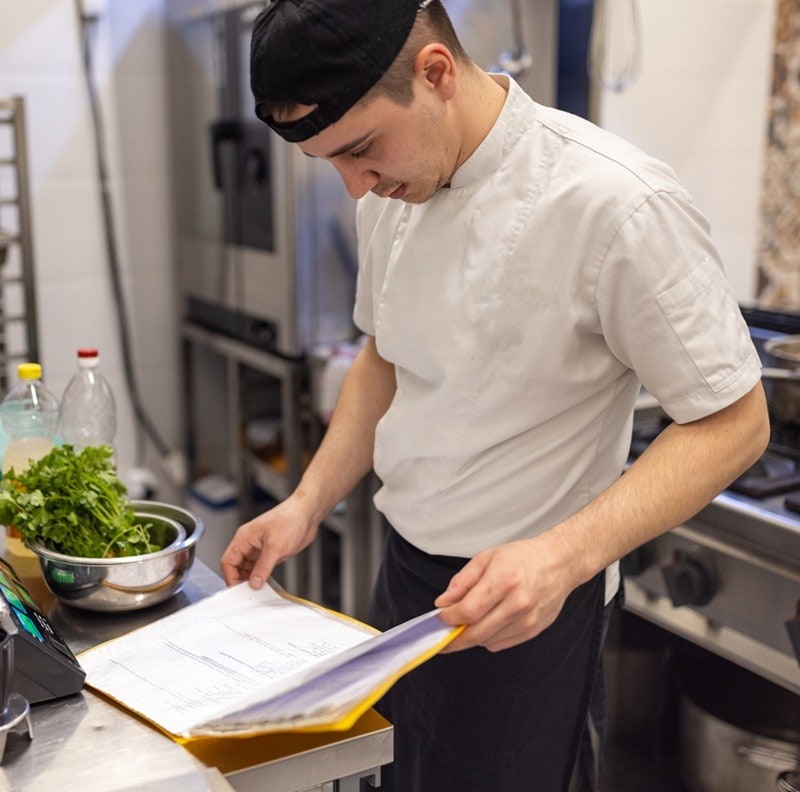 Un cocinero profesional está revisando notas en su cuaderno en el entorno de trabajo: su cocina. Un cocinero profesional está revisando notas en su cuaderno en el entorno de trabajo: su cocina.