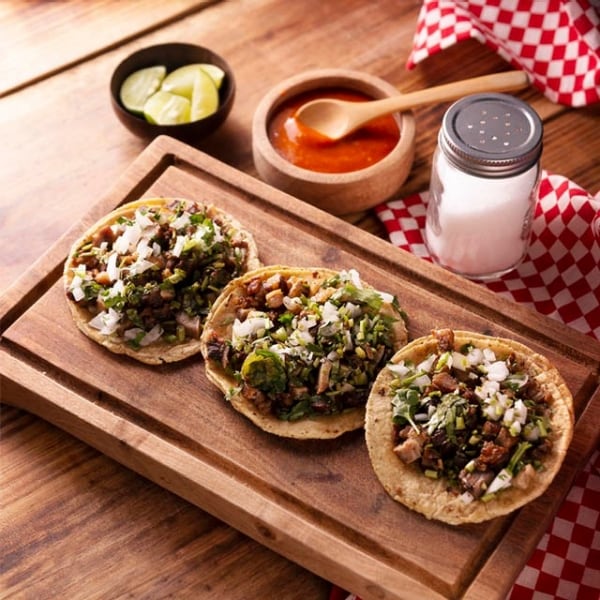 Tres tacos de suadero en tortillas de maíz sobre tabla de madera, comida callejera mexicana