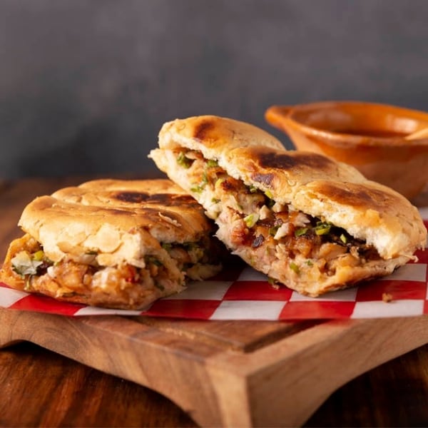 Torta de suadero sobre bandeja de madera, sandwich de res con pan telera cortado a la mitad, comida tipica mexicana