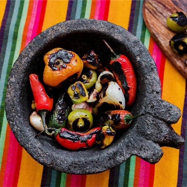  mortero mexicano con vegetales tatemados, chiles y cebollas quemados,    e ingredientes para salsa, sobre mantel de colores  