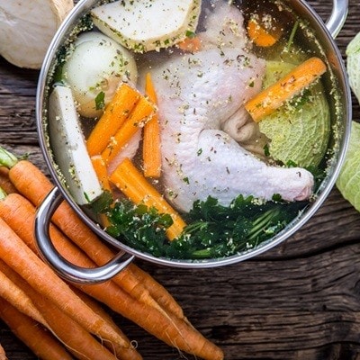 Top view of chicken soup -  broth on wooden table with vegetable.