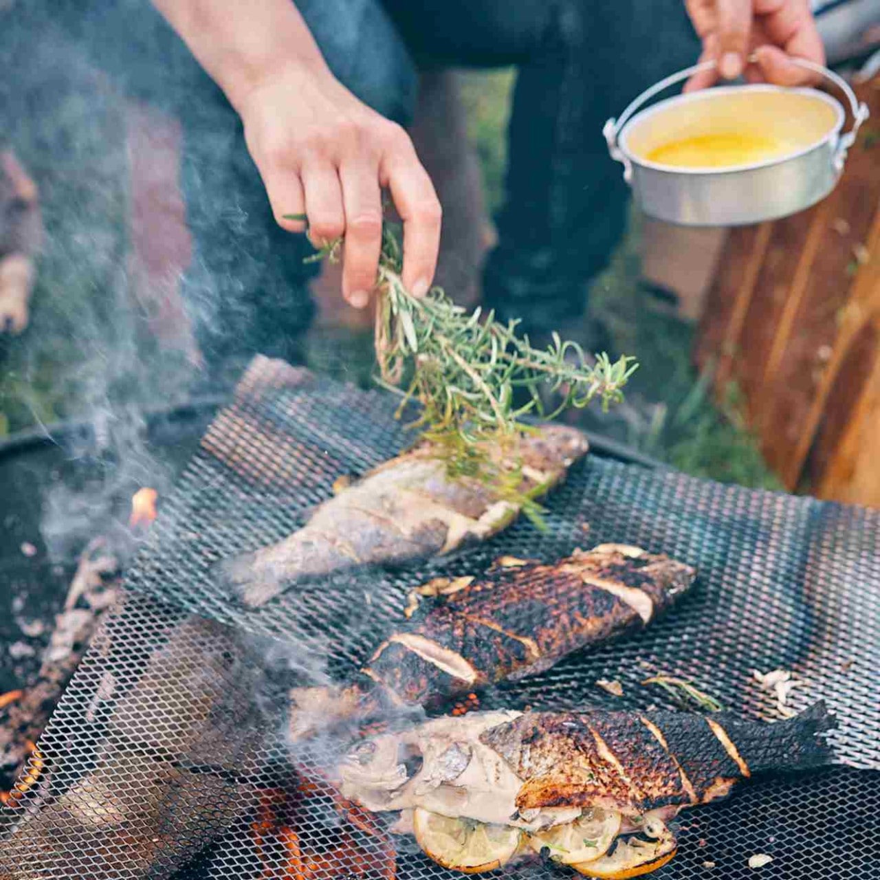 La mano de un hombre adereza un pescado ahumado a la parrilla utilizando una rama de romero. La mano de un hombre adereza un pescado ahumado a la parrilla utilizando una rama de romero.