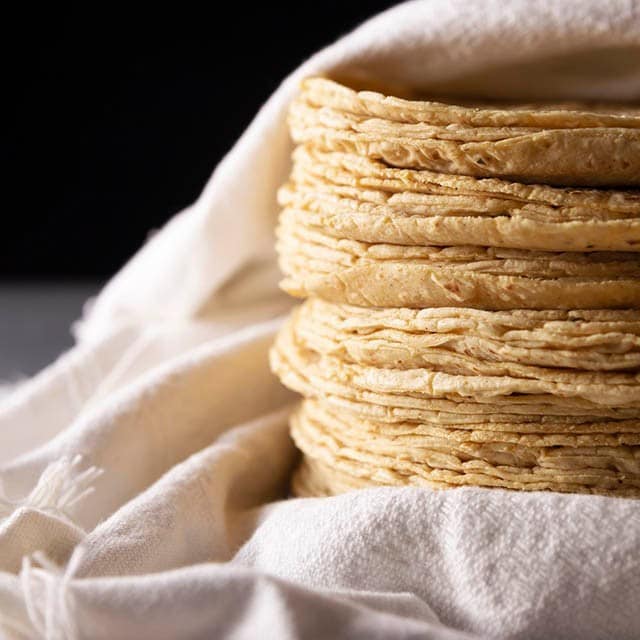 Pila de tortillas de maíz sobre paño de tela blanco. 