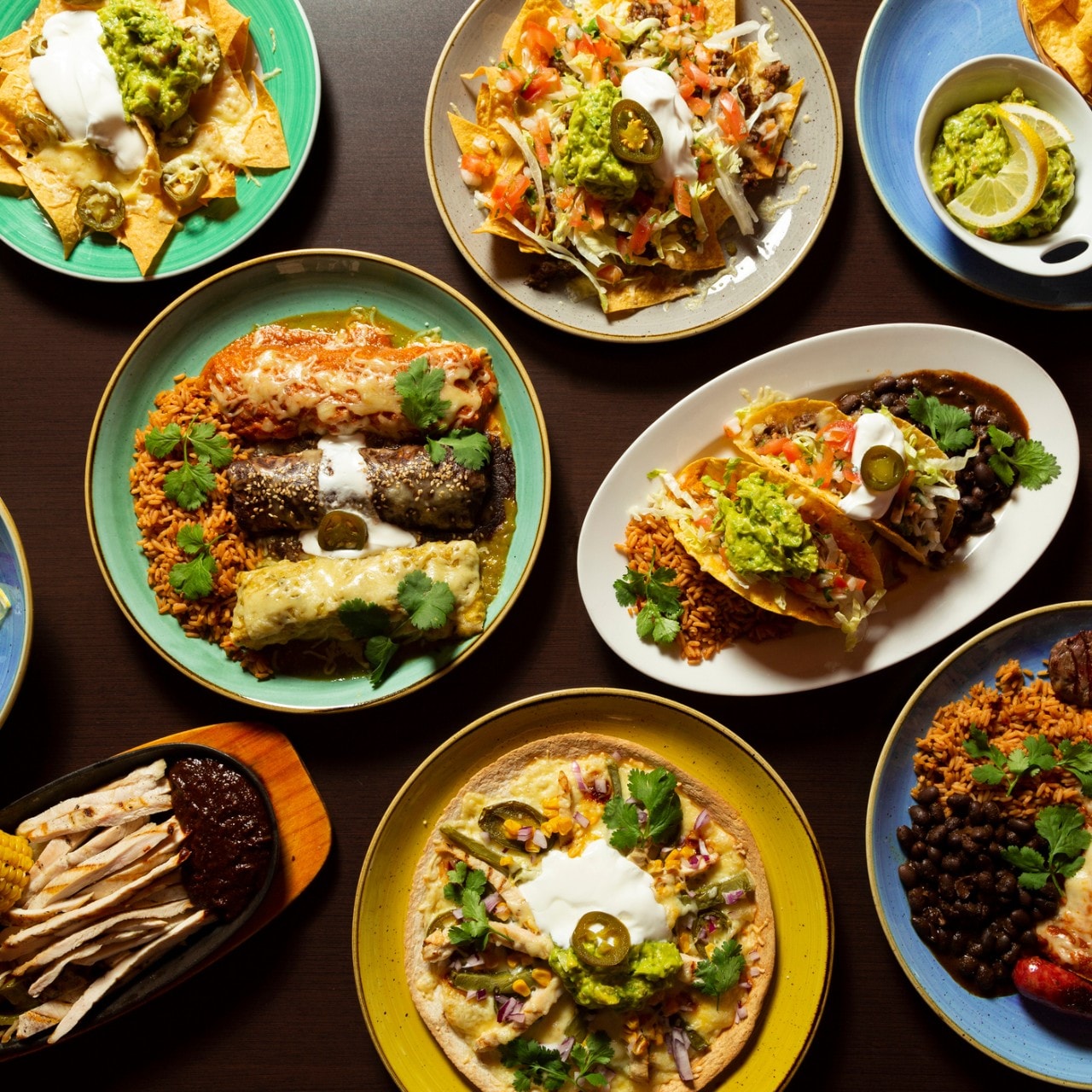 Table with typical mexican food, tacos, tamales, guacamole, tostadas, fajitas, top view on wooden background
